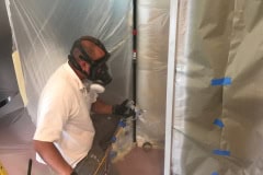 Professional cabinet painter spraying factory finish on kitchen cabinets during refinishing project in Groton MA