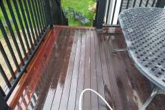 Outdoor balcony with newly stained wooden deck and metal table.