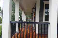 Porch wood flooring installation by Finish Masters, featuring polished wooden planks and black metal railing.