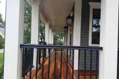 Professional hardwood porch flooring installation on a residential home with black metal railing and exterior lighting.