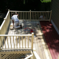 Professional deck painting by Finish Masters Construction & Painting. Workers painting a wooden deck on a residential porch.