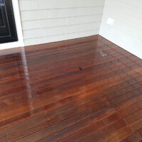 A beautifully refinished and stained wooden deck, enhancing the home's outdoor space with a polished look. Newly stained wooden deck with a glossy finish outside a house.