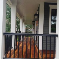 Porch wood flooring installation by Finish Masters, featuring polished wooden planks and black metal railing. Professional porch wood flooring installation with polished wooden planks.
