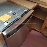 Professional kitchen appliance installation by Finish Masters. Dishwasher being installed under a wooden countertop in a kitchen.