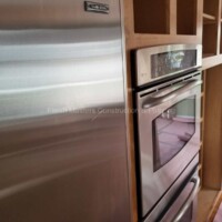 Quality kitchen appliances with wooden cabinetry for a stylish, functional space. Stainless steel refrigerator and oven installed in a contemporary kitchen setting.