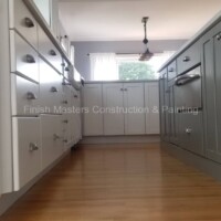 Beautifully renovated kitchen featuring sleek white and gray cabinets and warm hardwood floors by Finish Masters Construction & Painting. Modern kitchen with white and gray cabinetry and hardwood flooring.