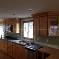 A newly renovated kitchen featuring custom wood cabinets, a stainless steel dishwasher, and a large window for natural light. Kitchen renovation with custom wood cabinets and modern appliances.