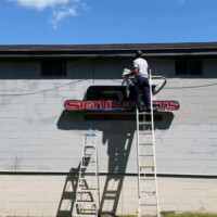 Professional exterior painting and signage installation by Finish Masters Construction & Painting. Workers painting exterior sign on commercial building.
