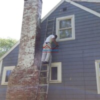 A worker painting the exterior of a blue house, showcasing quality craftsmanship and attention to detail. Professional house painting and exterior renovation by Finish Masters Construction & Painting.