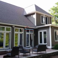 Beautifully painted house exterior with large windows and a cozy outdoor seating area, showcasing professional painting services. Modern house with fresh exterior paint and large windows in a lush green setting.