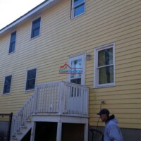 Skilled painters applying fresh paint to a yellow residential house exterior. Exterior house painting by Finish Masters Construction & Painting professionals.