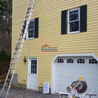 Skilled workers painting the yellow house exterior with ladders and equipment. Exterior house painting by Finish Masters professionals.