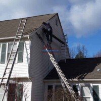 Skilled workers painting and repairing the exterior of a two-story house with ladders and safety gear. Professional exterior house painting and siding repair by Finish Masters.