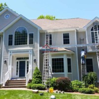Skilled painters working on the exterior of a large, beautiful home with ladders and painting tools. Professional exterior house painting by Finish Masters Construction & Painting.