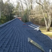 New dark blue roof with skylights and chimney in a wooded area.