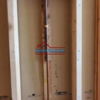 Interior view of wall framing with plumbing pipes installed, showcasing construction and renovation work. Framing and plumbing installation in a construction wall.