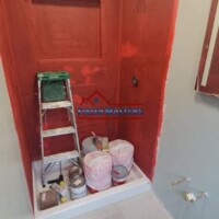 Interior bathroom wall being prepared for painting with primer and tools visible. Bathroom wall renovation with primer and paint application.