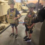 Two young boys in military costumes exploring a military display with tanks and vehicles. Children dressed as soldiers at a military exhibit.