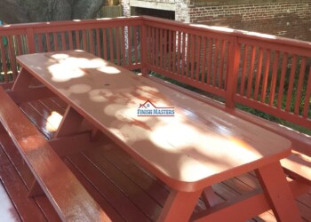 A sturdy wooden picnic table with attached benches, freshly stained and installed on a backyard deck for outdoor gatherings. Picnic table with attached benches on a wooden deck, finished with a glossy stain.