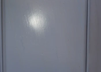 The details matter. Every imperfection revealed by primer is addressed and sanded smooth before the final finish is applied. Primed cabinet drawer front being inspected and sanded for a flawless finish