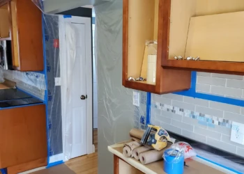 Every successful cabinet refinishing project starts with meticulous preparation. Protective coverings, masking, and door removal help ensure a clean, professional result. Kitchen cabinet refinishing preparation in Tewksbury Massachusetts showing floor protection masking and cabinet door removal before sanding and painting.