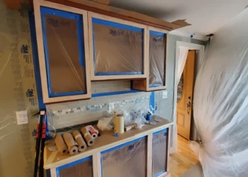 Professional results require professional containment. Dust barriers, masking, and surface protection are in place to ensure a clean application and a flawless factory-quality finish. Finish Masters cabinet refinishing project in Tewksbury Massachusetts showing cabinet boxes masked, dust barriers installed, and plastic containment sheeting in place before primer application.