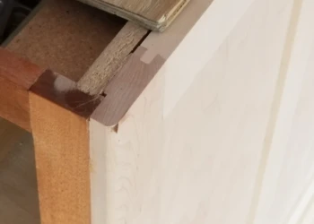 Close-up of cabinet corner being sanded and prepared for refinishing.