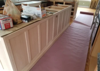 Kitchen cabinets being refinished with a protective covering on the floor.