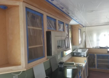 Kitchen cabinets being refinished with protective plastic on the windows.