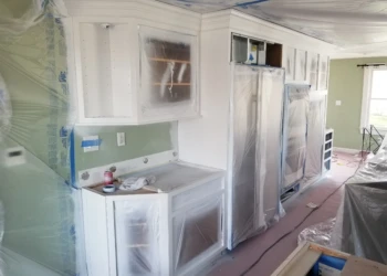 Kitchen cabinets being refinished and protected with plastic sheeting.