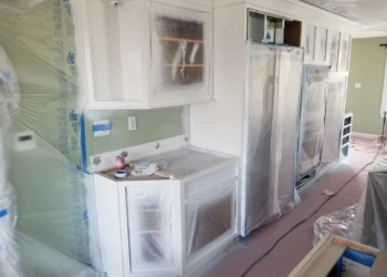 Kitchen cabinets being refinished and protected with plastic wrap.