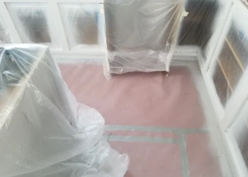 Cabinet refinishing process with plastic coverings in a home kitchen.