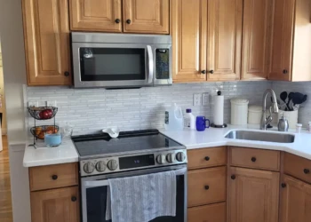 Before the transformation. These original maple cabinets featured the warm amber tones that were popular years ago, but the aging finish had begun making the kitchen feel dated and darker than the homeowners desired. Finish Masters cabinet painting project in Burlington Massachusetts showing original maple kitchen cabinets with an aging amber polyurethane finish before painting in Benjamin Moore AF-70 Storm.