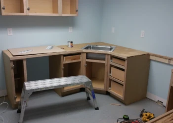 Unfinished wooden kitchen cabinets installed in a basement corner with a metal step stool and power tools on the floor