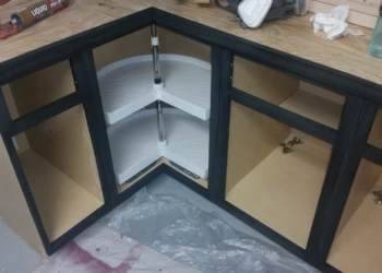 Corner kitchen cabinets with black painted oak frames and unfinished interiors in a basement kitchen installation