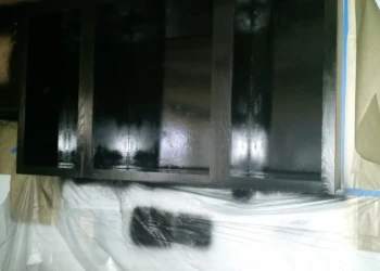 Matte black painted oak kitchen cabinets installed in a basement kitchen with plastic protective covering