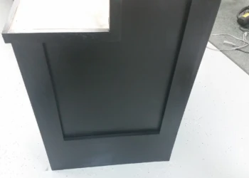 Close-up of a matte black painted oak cabinet door with recessed panel and white countertop edge in basement kitchen in Billerica MA