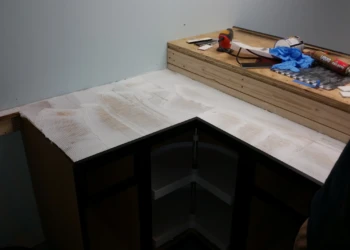 Corner base cabinets installed in a basement kitchen with tools and materials on an adjacent ledge in Billerica MA