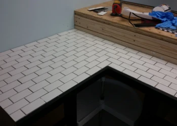 Close-up of white rectangular tiles neatly installed on a basement kitchen countertop with black grout and unfinished wooden backsplash