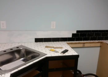 Partially installed black painted oak cabinets with white and black tiled countertop in a basement kitchen in Billerica MA