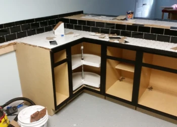 Black painted oak kitchen cabinets in a basement with open cabinet doors showing interior shelving and black tile countertop