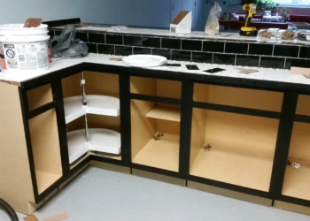 Partially installed matte black painted oak base cabinets with open shelves and visible interiors in a basement kitchen.