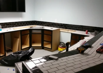 Basement kitchen under renovation showing cabinetry painted black with wood interiors and black and white tiled countertops