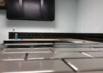 Close-up view of matte black painted oak kitchen cabinets and glossy black tile backsplash in a basement kitchen