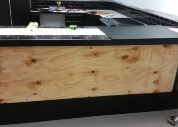 Black painted oak cabinets under a tiled counter with black subway tile backsplash in a basement kitchen in Billerica, MA