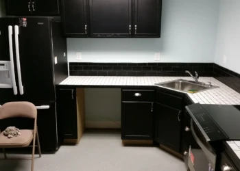 Basement kitchen with black painted oak cabinets, white tiled countertop, stainless steel sink, and black appliances in Billerica MA
