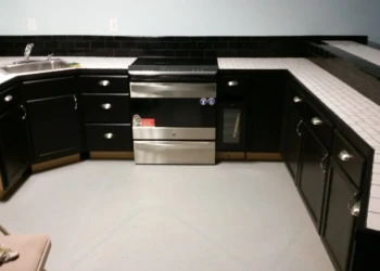 Black painted oak kitchen cabinets with silver handles and white tiled countertops in a basement kitchen in Billerica MA