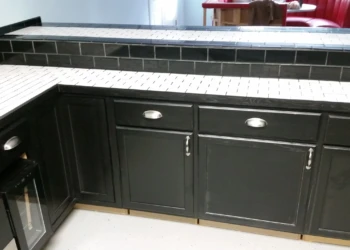 Black painted oak cabinets with silver handles under white tiled countertop in basement kitchen