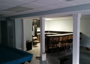 Basement kitchen featuring black painted oak cabinets and a wraparound counter with bar stools in Billerica MA