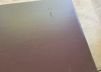 Close-up of a brown bathroom cabinet door panel with a smooth, stained finish showing minor surface texture and a few imperfections.